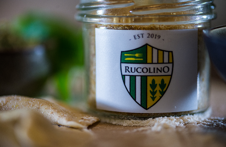 Image, Vous pouvez voir un pot de confiture avec du vermigiano, une variante végétalienne du parmesan à base de noix de cajou et d'amande, que Rucolino a fabriquée lui-même. Sur le verre, vous pouvez voir le logo Rucolino.