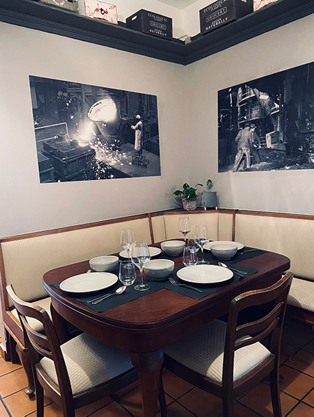Image, La table chez Rucolino est dressée. Espace pour 4 avec 2 chaises et un banc dans le coin en arrière-plan accrocher deux images en noir et blanc.