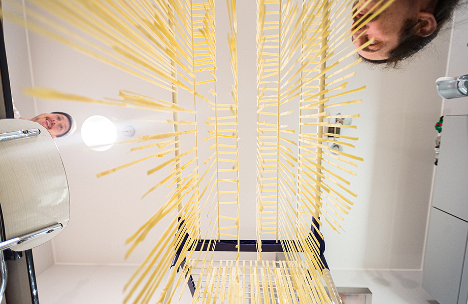Image, Les linguine sont suspendus sur des fils à linge pour sécher. La photo regarde de bas en haut les linguines suspendus, vous pouvez voir les visages de deux cuisiniers à gauche et à droite sur le bord.