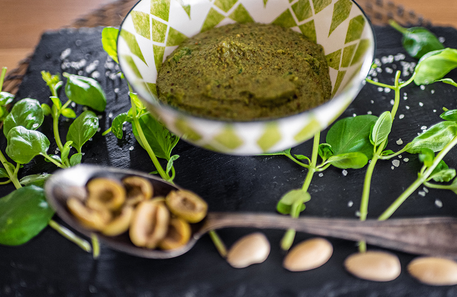 Image, Composition d'un pesto de basilic frais, olives, pistaches et amandes dans un bol. Devant elle se trouve une cuillère avec des amandes et les deux Steet sur une assiette en ardoise.